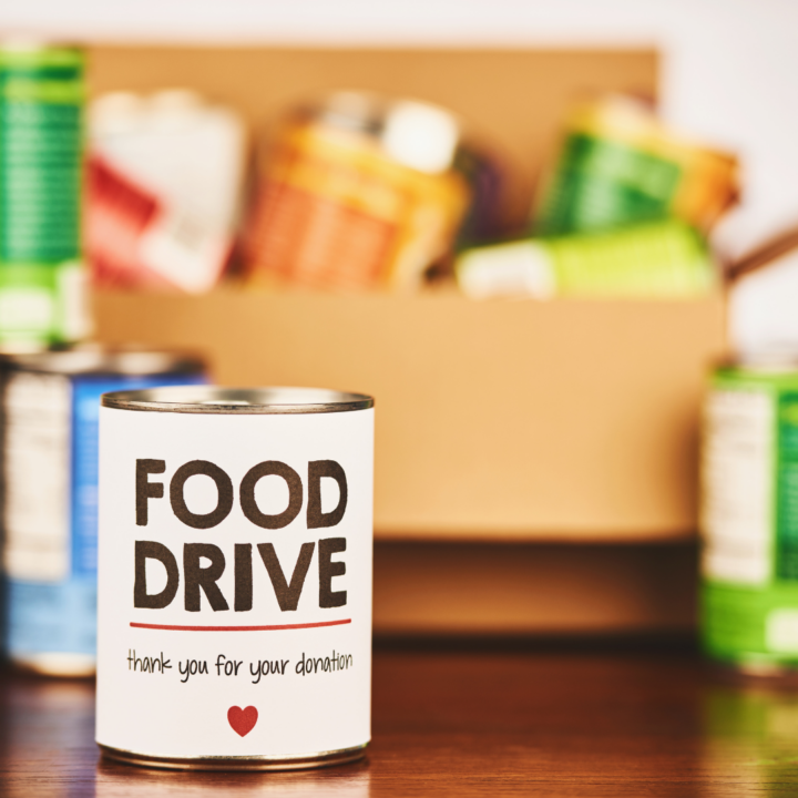 Can that says food drive in front of a box of canned foods